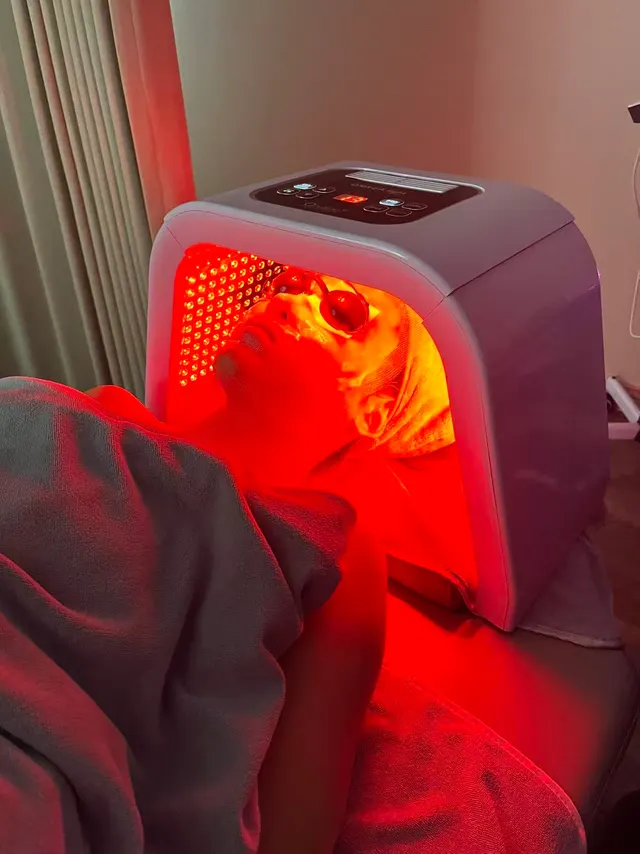 A client in protective goggles lying under a red LED light therapy panel during a facial at O2 Head & Beauty Spa in Arcadia
