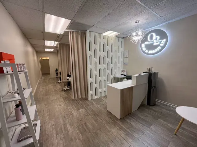 Reception at O2 Head & Beauty Spa in Arcadia: a white desk beneath the lit O2 sign, with curtained treatment bays along the corridor